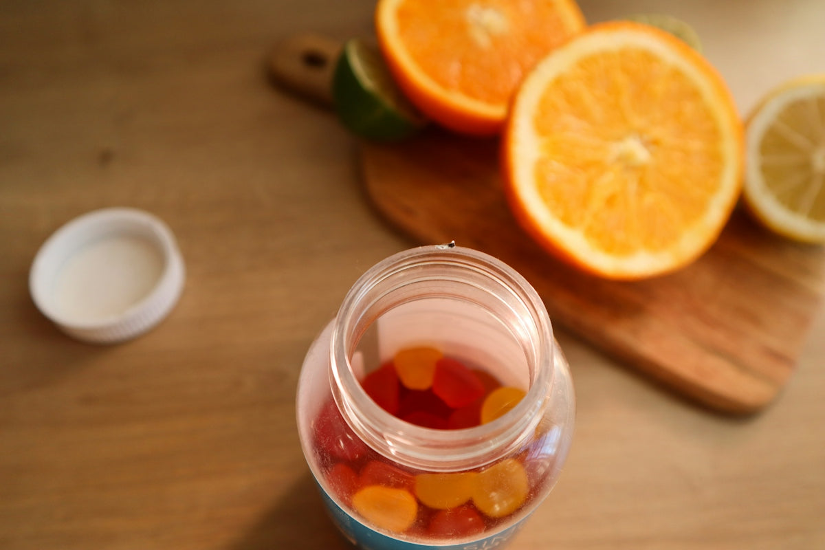 a jar filled with gummy bears next to sliced oranges